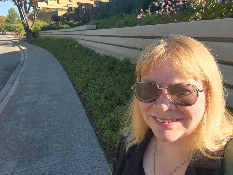 Kate is a middle aged blonde woman smiling in the sunlight and wearing sunglasses.