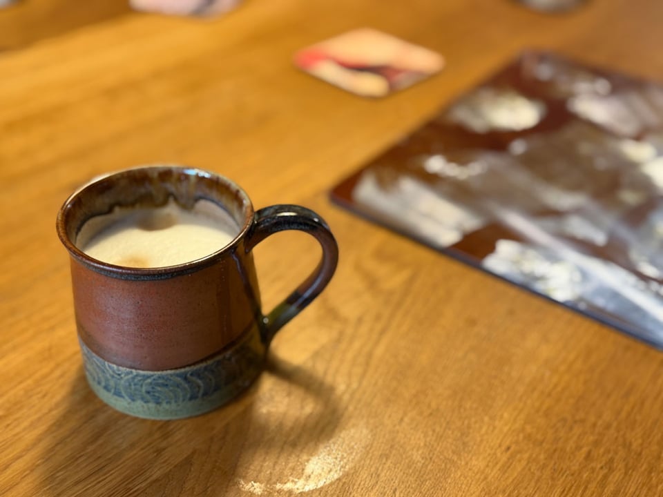 A brown handmade ceramic mug is filled with a cappuccino.