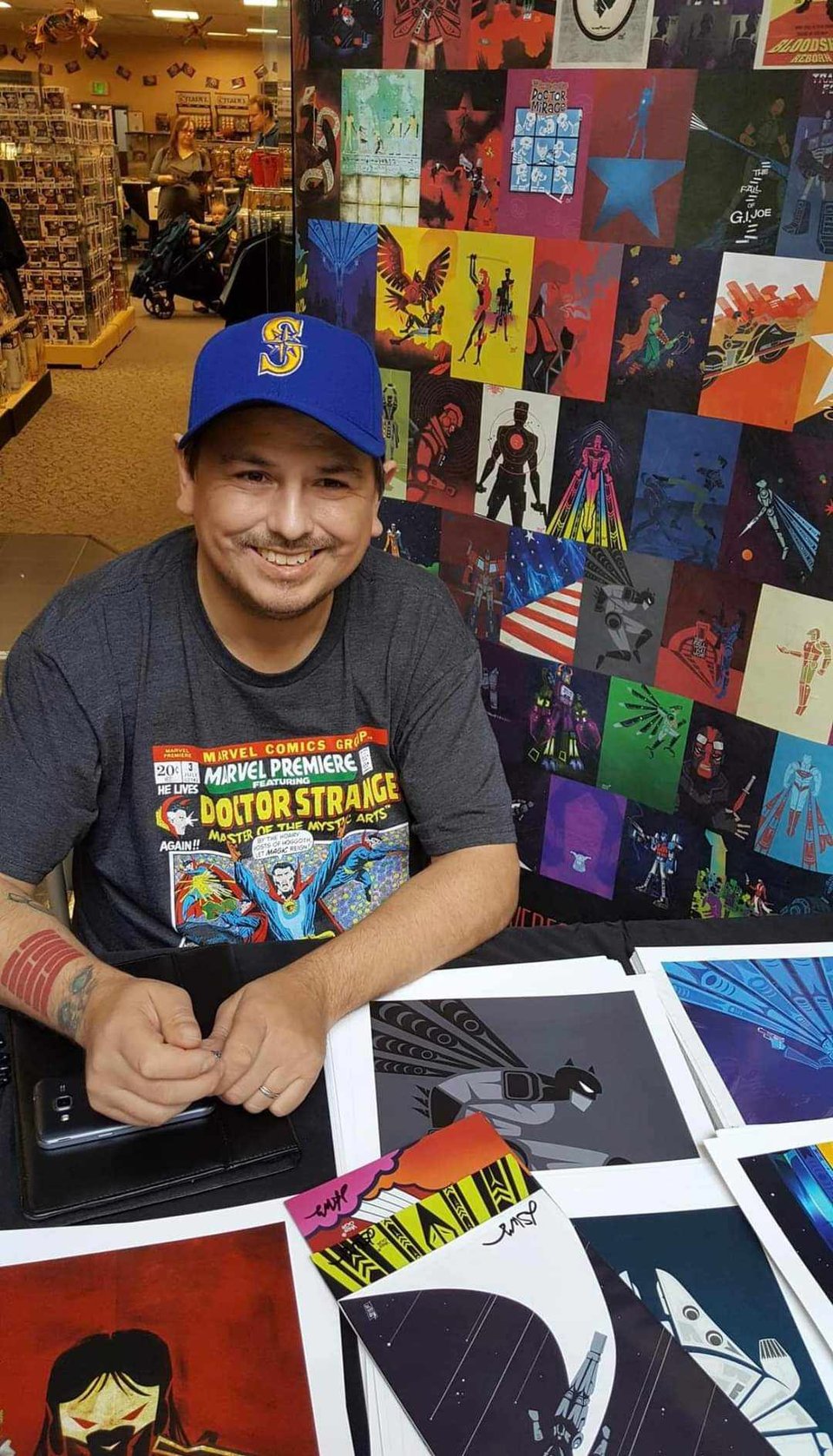 A photo of Jeffrey Veregge, smiling and surrounded by prints of his art.