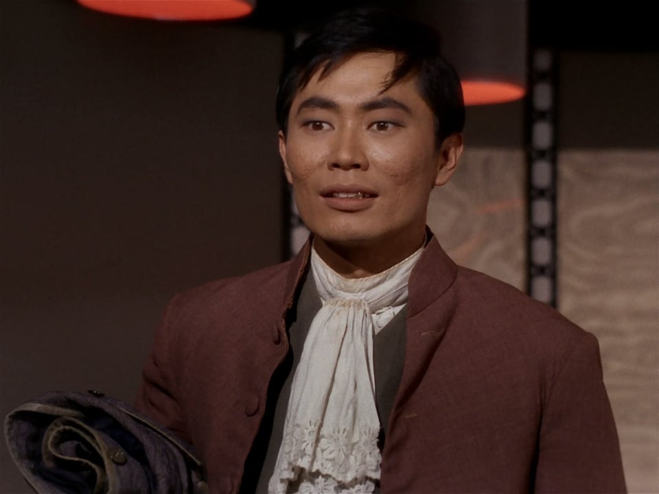 An image of Sulu from the opening moments of Star Trek, "Return of the Archons." He's wearing an old-timey outfit with a lacey scarf, and he has a blissed-out look because he's gotten brainwashed by Landru
