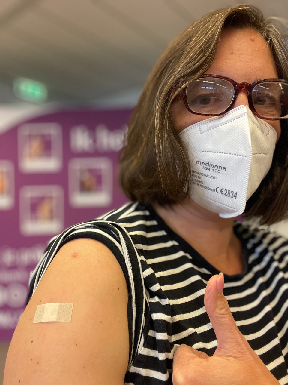 A woman wearing glasses and a mask shows off her bandaid on her upper arm after getting vaccinated.