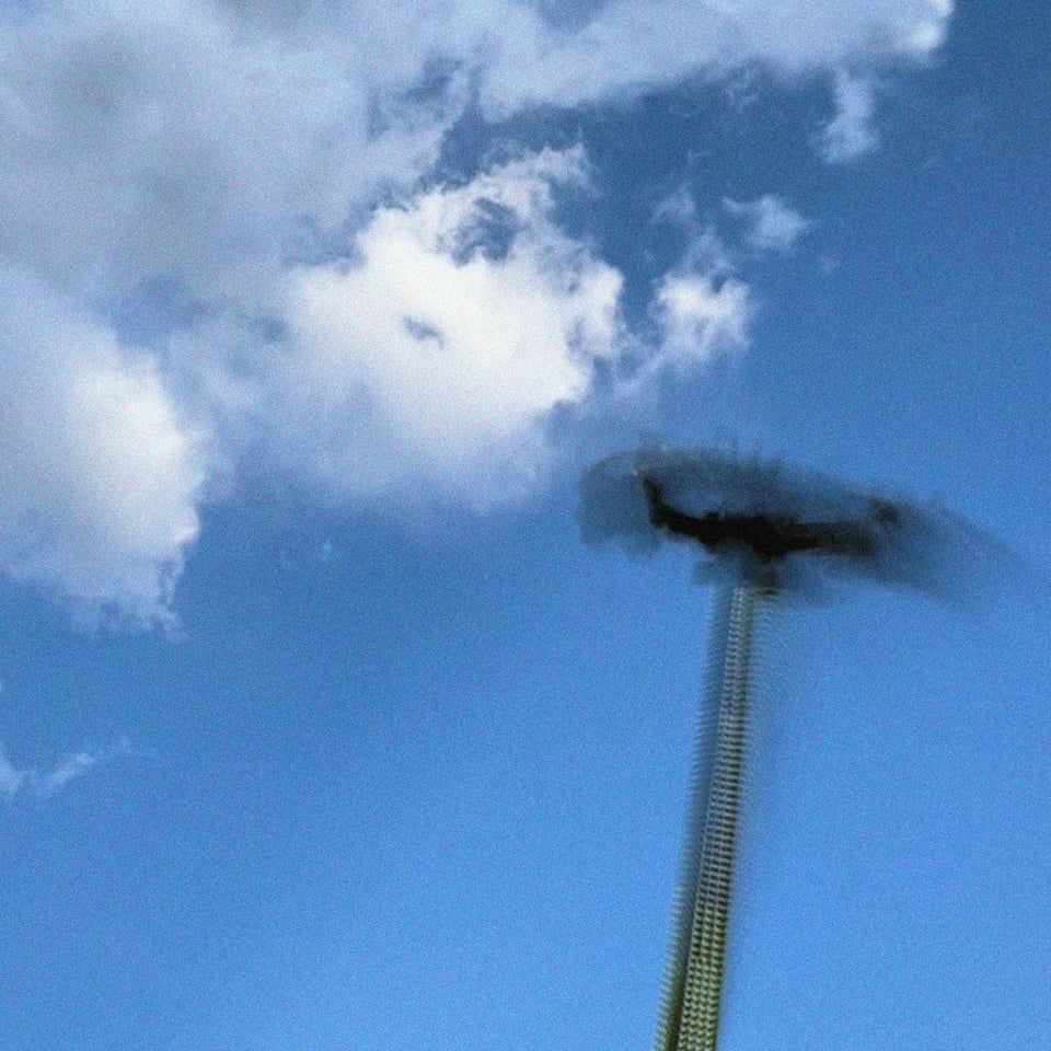 a tall fair ride is captured mid inverted swing in a blur of motion against a brilliant blue sky