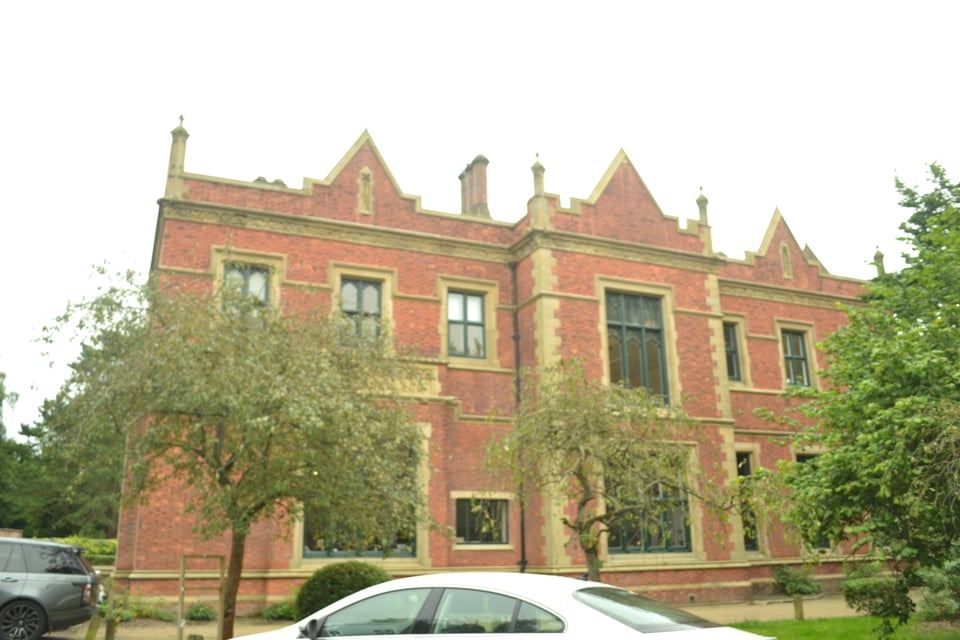 A stately red brick manor house under a gray sky, with gables and stone-framed windows.