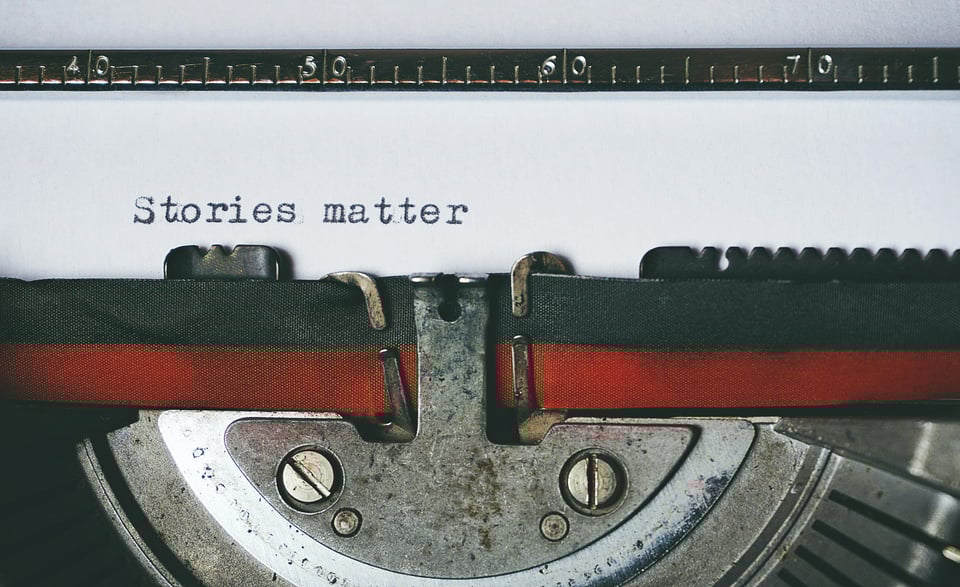 Up-close photo of a typewriter. There is a piece of paper in the typewriter with the words "Stories matter" typed on it.
