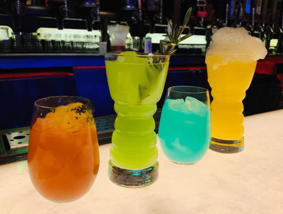 an image showing four cocktail drinks from oga's cantina in star wars galaxy's edge in walt disney world - a short orange drink, a tall lime green drink, a short blue drink and a tall foaming yellow drink
