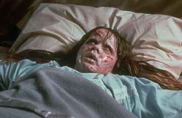 A girl lies in bed with a distressed expression and disfigured face, appearing to be experiencing a supernatural event.