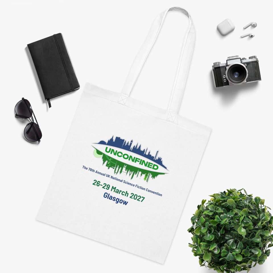 A white tote bag with the Unconfined logo on it, surrounded by several items: sunglasses, a notebook, a camera, and for some reason, a small plant.