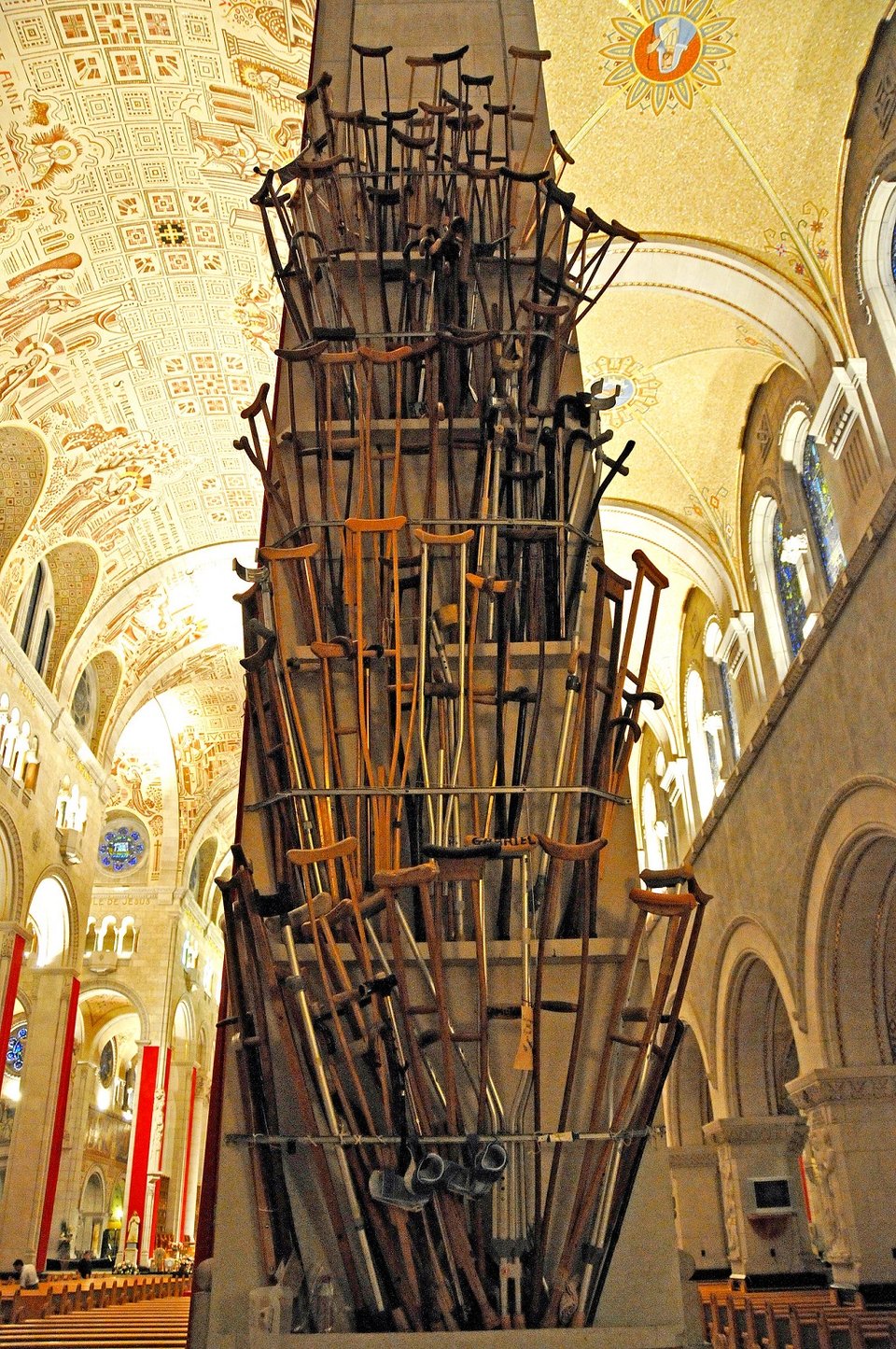 The inside of a church, with a column in the middle covered in crutches and canes in a way that almost makes it look like a large tree.