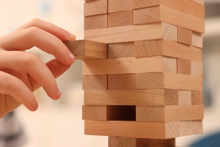 A close up of a Jenga tower. A hand is carefully removing one of its wooden pieces.