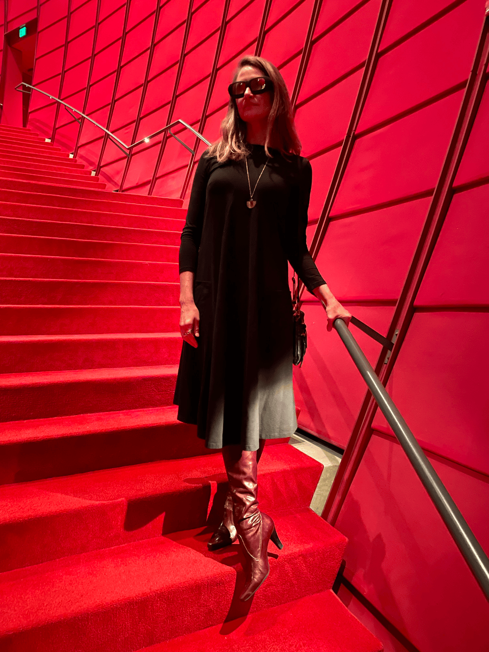 A beautiful woman wears a black dress and 3D glasses on a curving staircase covered in red carpet