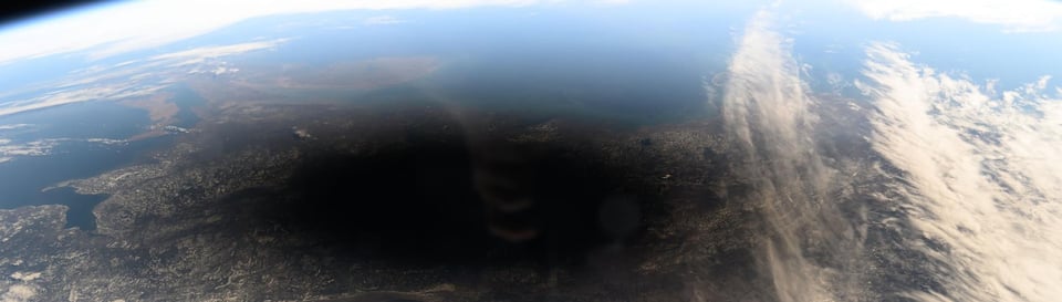 The earth from space, with a large shadow over a land mass and ocean