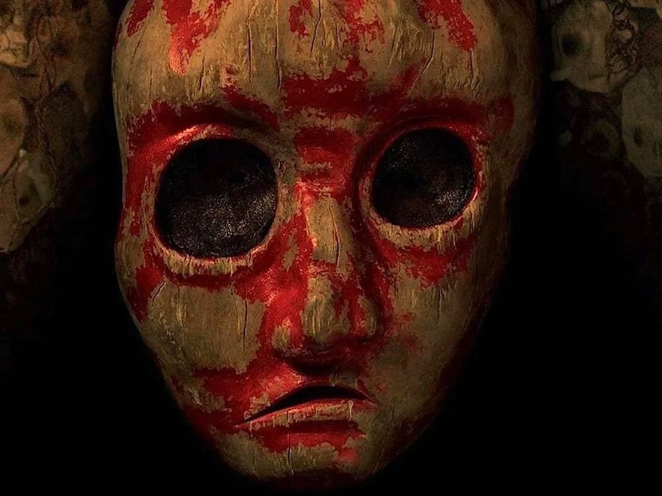 A gruesome blood-covered mask with large circular eyes from Noroi: The Curse