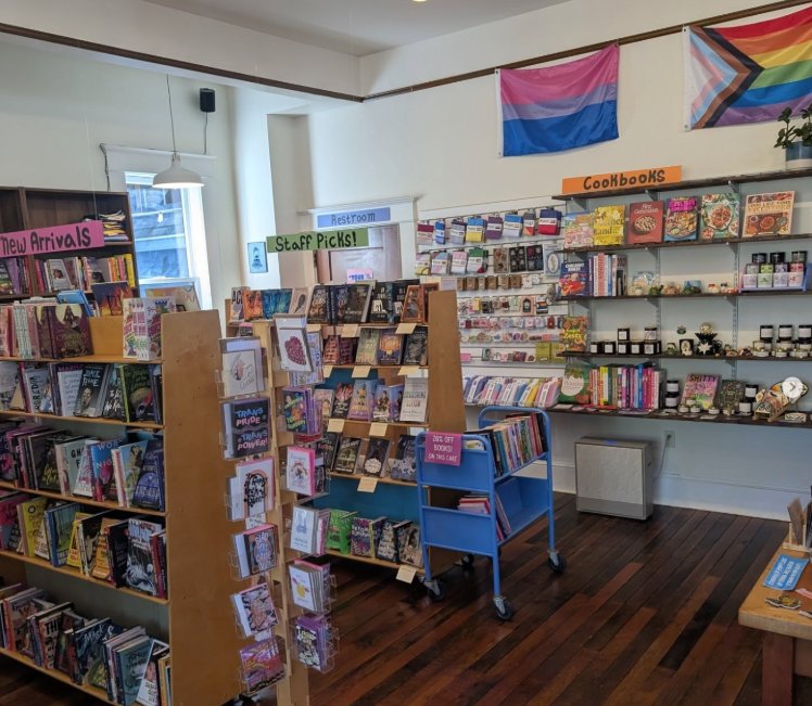 A bookstore space with queer flags, plus sections for cookbooks, new arrivals and staff picks