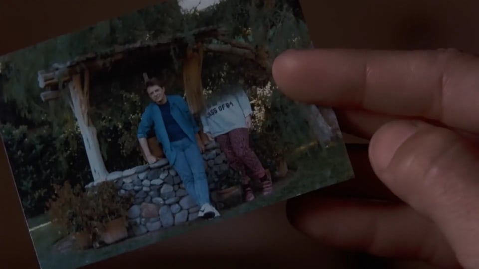 Marty holds up a photograph of himself and his two siblings. His brother's image is completely erased, and his sister's is halfway missing.