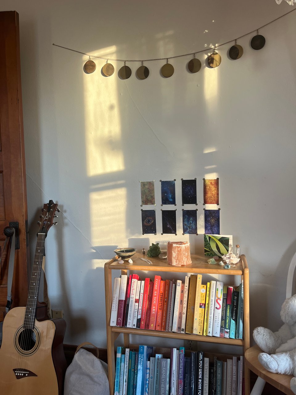 bedroom shot of guitar, meditation cushion, equinox altar, pinned up altar cards, hanging moon decoration, and partial sun on the wall
