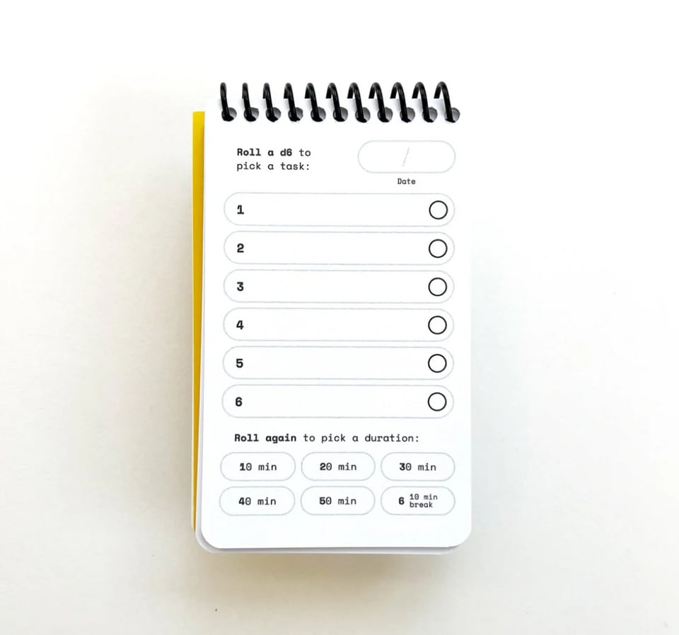 A picture of a small paper pad. On each sheet is printed six line items that are empty for the user to fill out. At the top of the sheet is the instructions "roll a D6 to pick a task". At the bottom of the page is the instructions "roll again to pick a duration", and there are six possible options here: 10 minutes, 20 minutes, 30 minutes, 40 minutes, 50 minutes, or a 10 minute break.