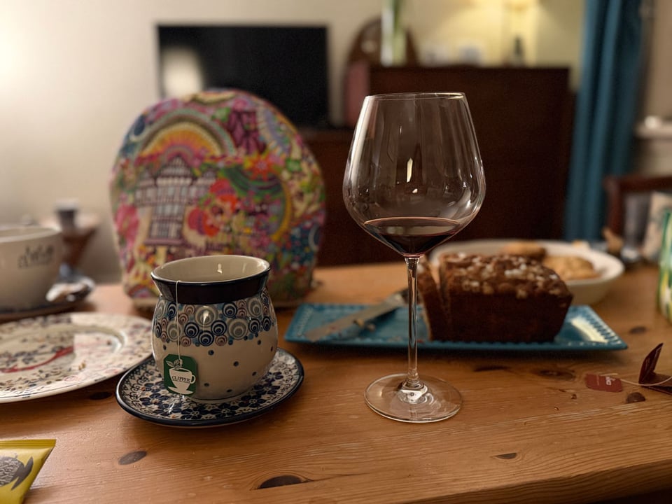 A coffee table is set with cups of tea, a glass of wine and a cake and cookies.