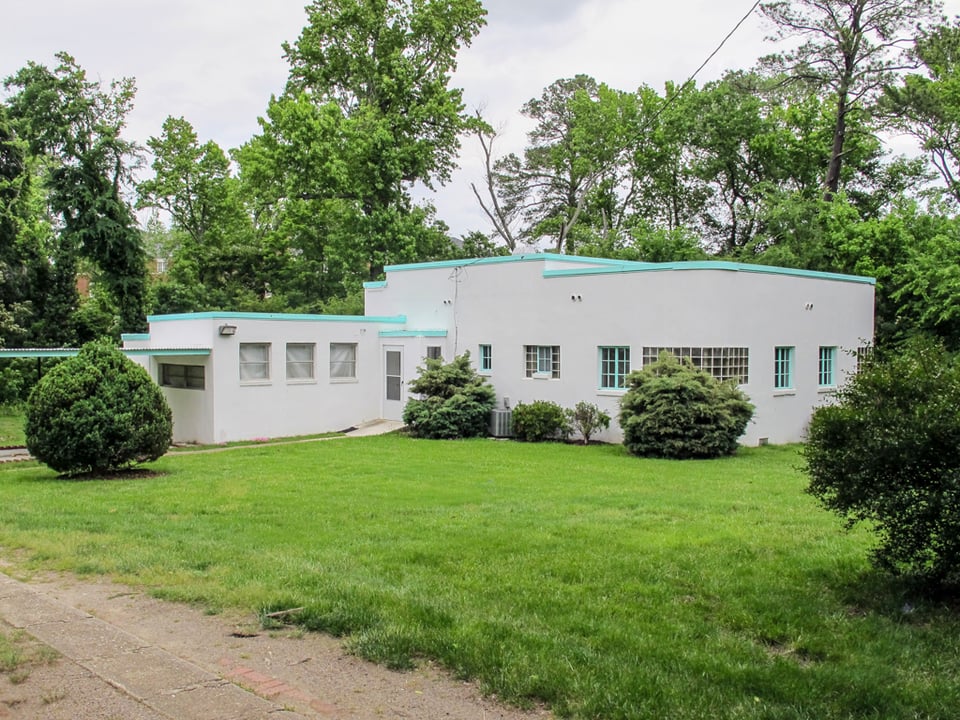 A white single-story house with a flat roof and trim painted a bright teal blue.