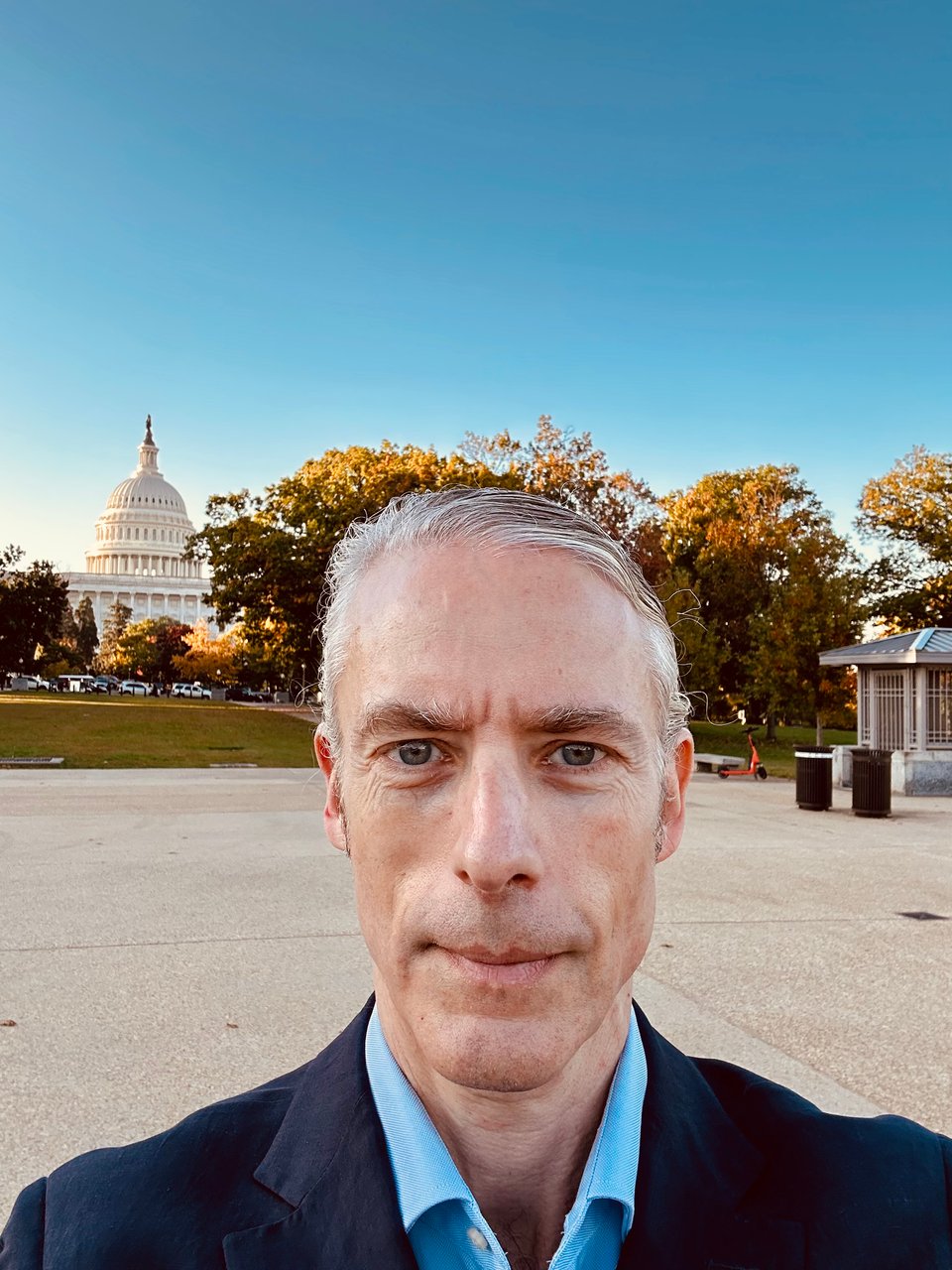 Selfie of white man in navy suit & blur dress shirt standing in front of the Capitol building