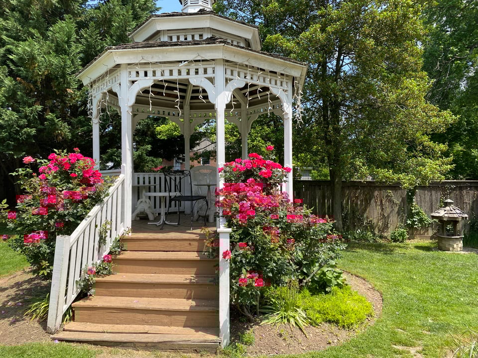 a white gazebo with flower bushes on each side of the stairs