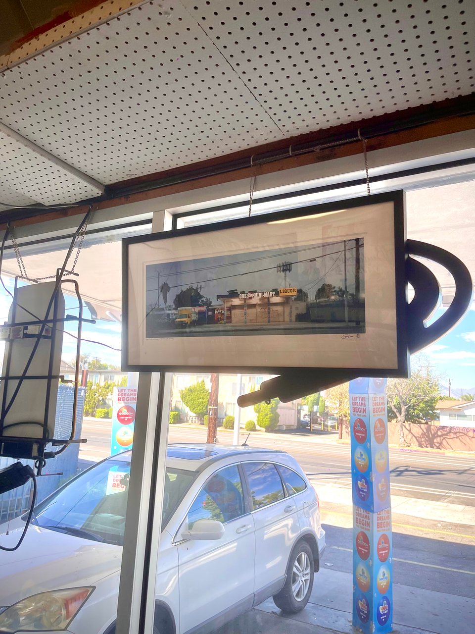 An iPhone snapshot of my printed and framed "One Stop Mini-Mart" artwork hanging on the wall of the mini-mart itself.