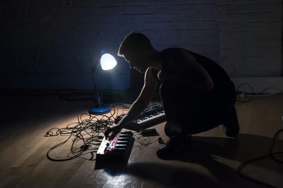 nora crouched in a dark corner of links hall in 2018, adjusting a dial on some sound equipment in the light of a small desk lamp.