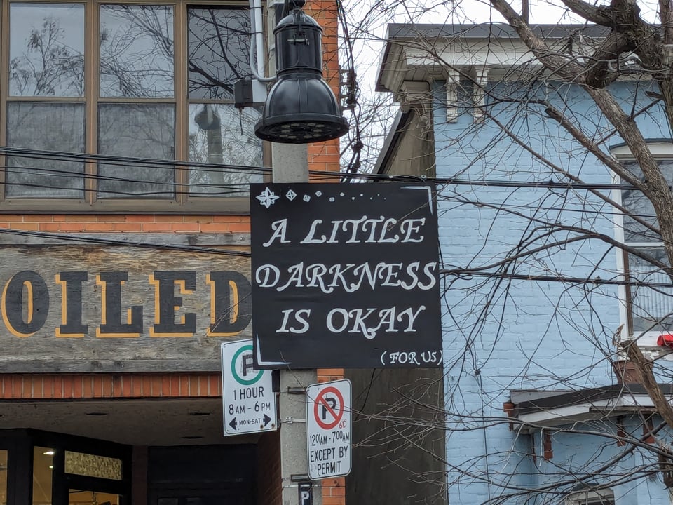 A sign posted in Toronto's Kensington Market, reading: A little darkness is okay (for us).