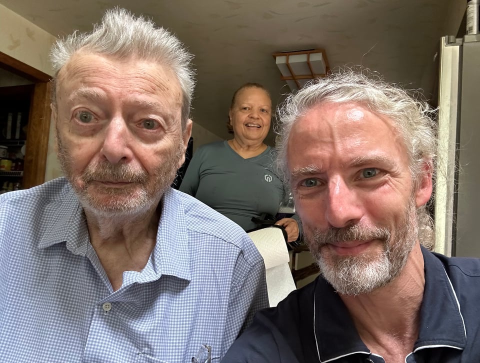 Photo of a father (87) and son (53), with the father's partner behind him
