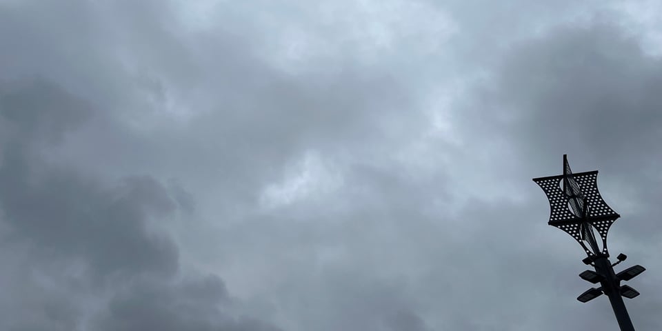 A metal light pole in silhouette against grey clouds. Photo: Lars Gotrich