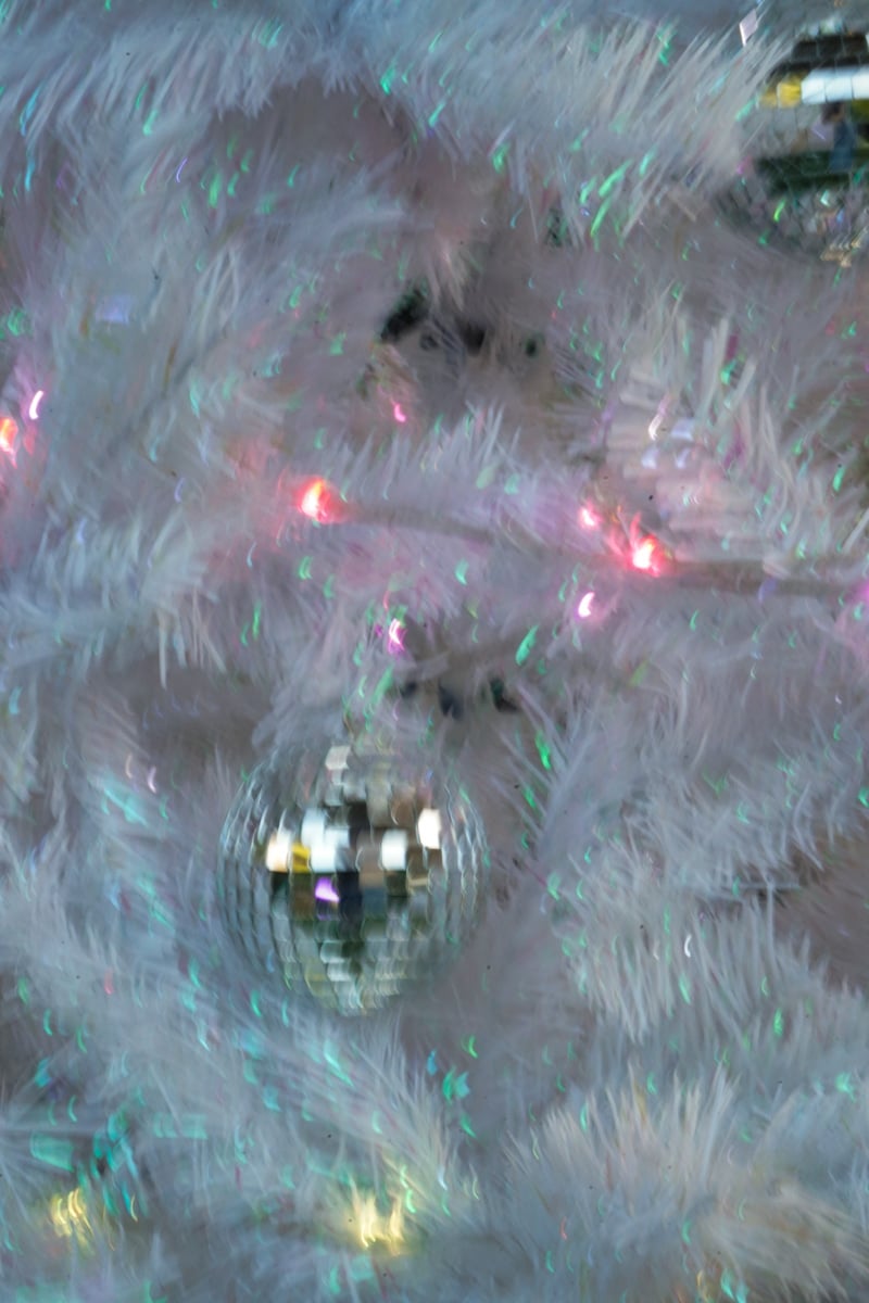 A blurry photo of a disco ball ornament on a white christmas tree