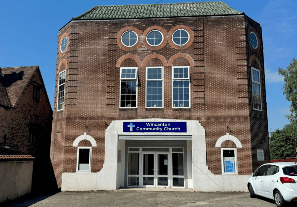 The Wincanton Plaza cinema. It's a 1930s brick building with Portland stone detailing. It has a squared off front with three large tall windows in the centre. Above those windows, three round windows are lined up. This design of a long window topped with a round one is replicated on the corner walls. A large sign announces its use as a church.
