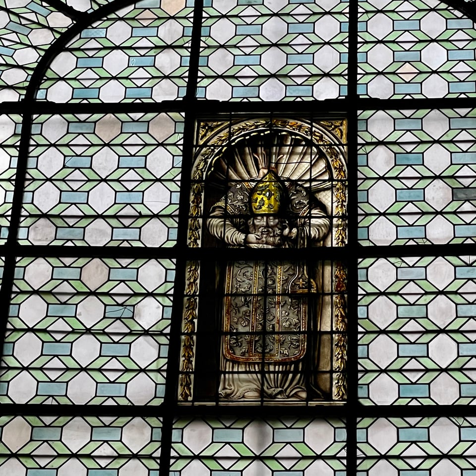 a man in a stained glass window holds his own severed head