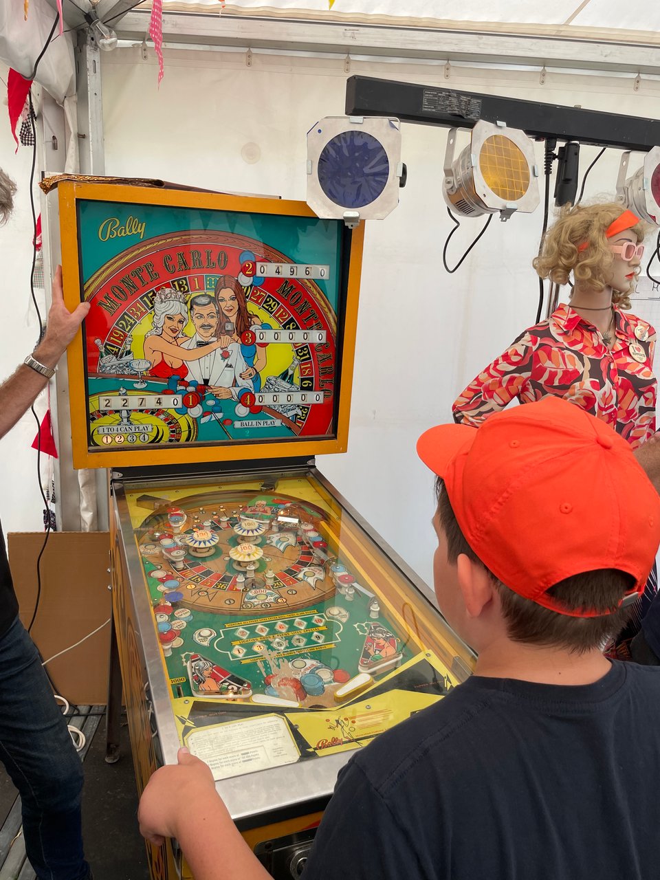 A boy in an orange baseball cap plays a vintage pinball machine.