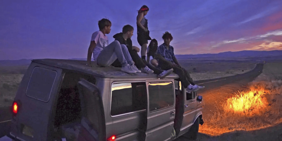 Five teenagers on top of a van with a purple sky.