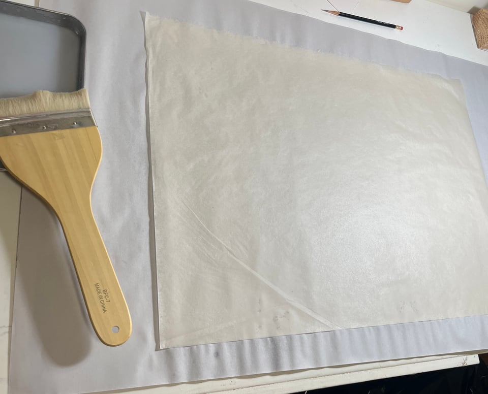 a brush is resting on top of a tray of milky substance next to a hair-thin sheet of japanese paper