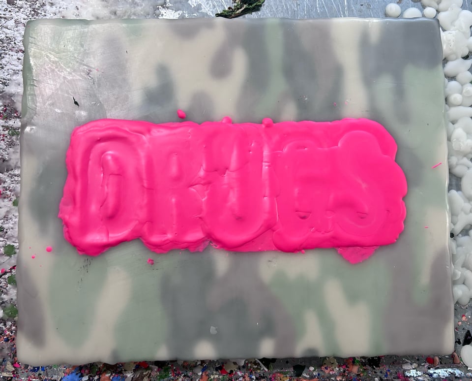 Painting in progress. Tiny fella. Background is camouflage. Big bright pink blob on top where you can kinda sorta see the word DRUGS underneath.
