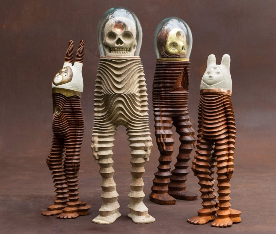 four wooden characters, two with astronaut-style masks and two with antennae