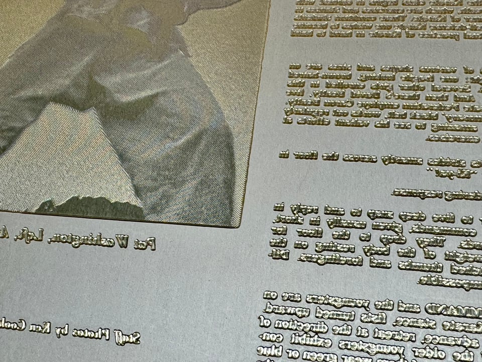 Detail of a flexographic printing plate, raised rubbery type, from 1973 showing an edge of a photo of a karate class and some text. The image has a gold hue.