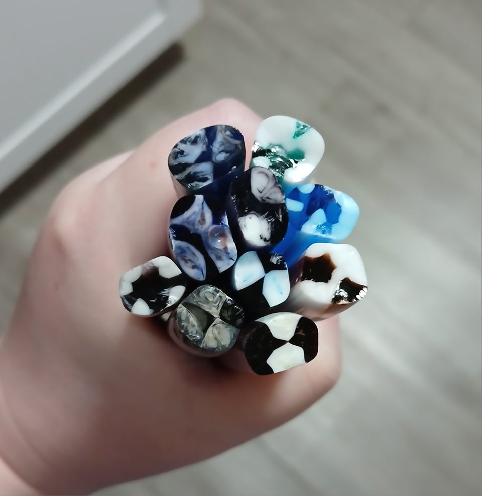 my hand holding a variety of glass rods with patterns inside made from layering rods and fusing them together
