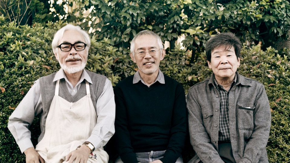 Three elderly Japanese men: left, with glasses, a short white beard, and a white apron, is Hayao Miyazaki; centre, in a black jumper and glasses, is Toshio Suzuki; right, in a grey jacket, is Isao Takahata