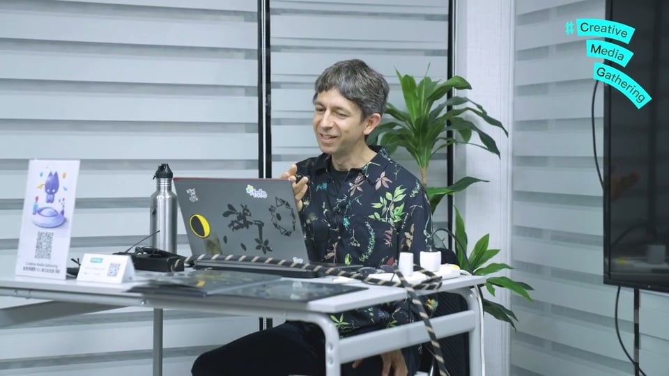 Abe sitting behind a desk and a laptop giving a talk to an audience in Taipei