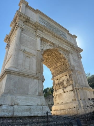 A close-up view of a stone triumphal arch with ornate carvings and inscriptions against a clear blue sky.