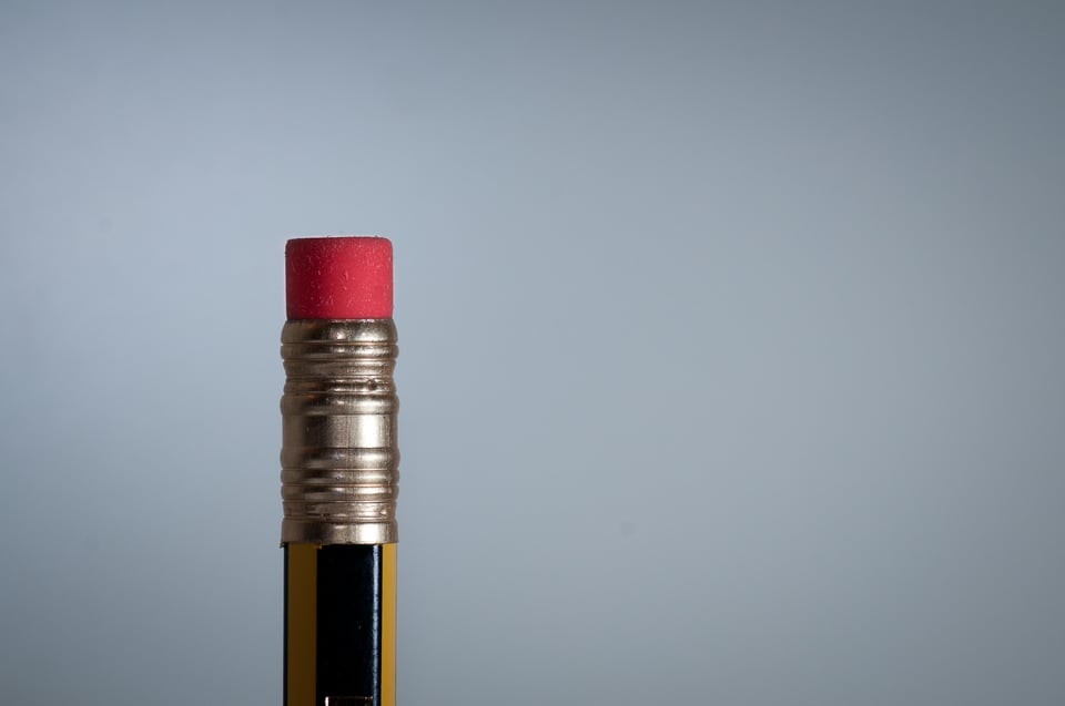 A closeup of the end of a pencil, showing the metal ferrule and the pink eraser. The pencil is painted yellow and black, and the background is grey
