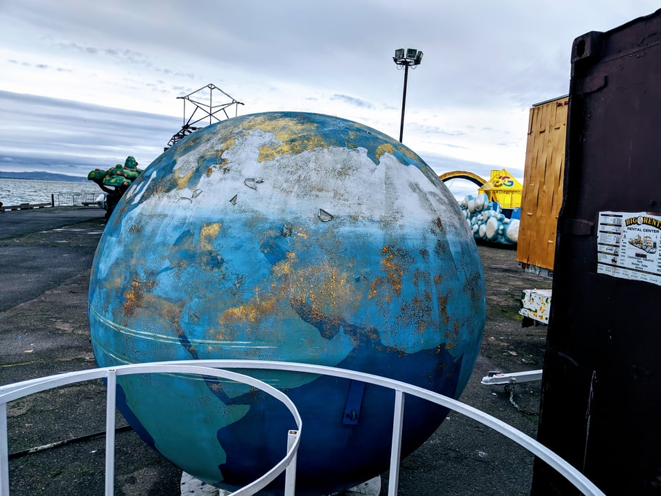 A weirdly fucked up, rusted, weather-worn globe of the planet Earth. It's one of the old parade floats on a pier in San Francisco that are just left out exposed to the elements.