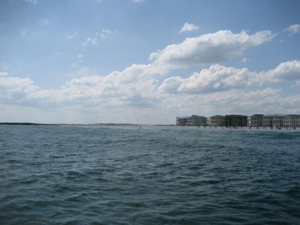 Open ocean. It ends at a sandy beach and square buildings with lots of windows.