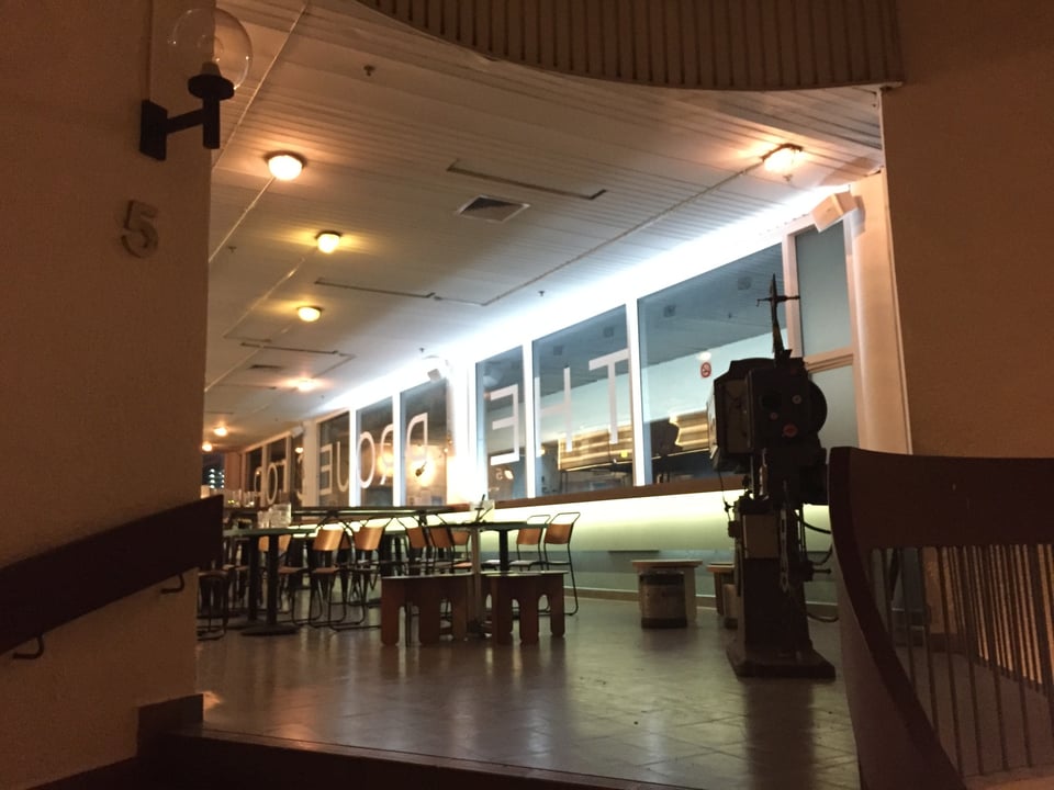 The Projector's lobby, empty except for its tables on chairs. The cinema's name is pasted on the windows, but in reverse.