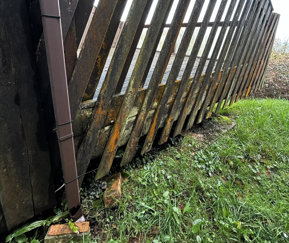 Detail of the side of a balcony close to the ground. The diagonal slats of the privacy screen are covered in green and orange mold. It's so thick you can smell it.
