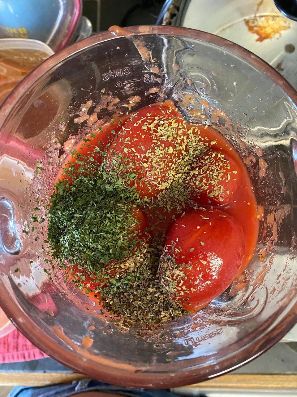 A photo taken from above of a glass blender with peeled tomatoes and spices