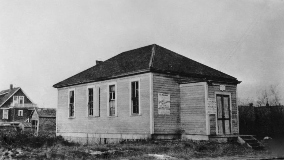 Black and white photo of a small building with four windows along one side.