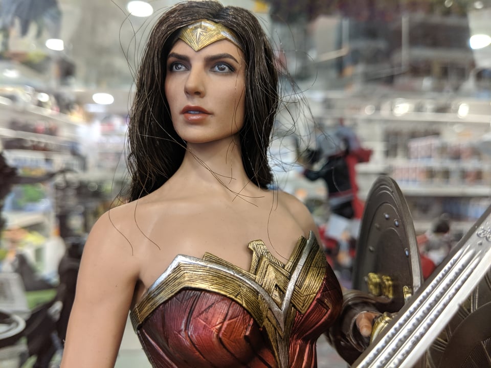 A statue of Wonder Woman at a science fiction convention. She has a dead eyed look, like she has seen things she cannot unsee. She's holding a sword and shield
